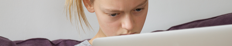 Ein junges Mädchen blickt genervt auf einen Laptop-Bildschirm.