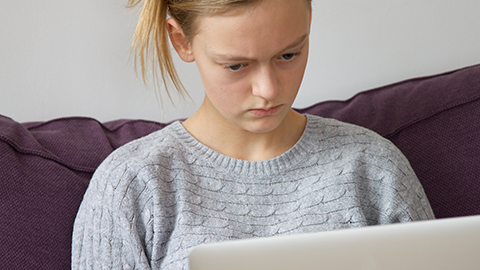 Ein junges Mädchen blickt genervt auf einen Laptop-Bildschirm. (Link zu Informationen über Digitale Gewalt)